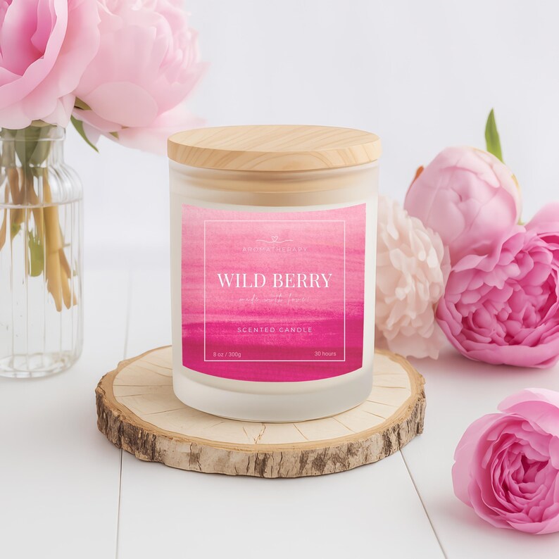 Może przedstawiać: Świeca zapachowa Wild Berry z drewnianą pokrywką, prezentowana na drewnianym plastrze. Etykieta zawiera akwarelowy wz&oacute;r w odcieniach r&oacute;żu i napis "Wild Berry". Świeca otoczona jest r&oacute;żowymi piwoniami.