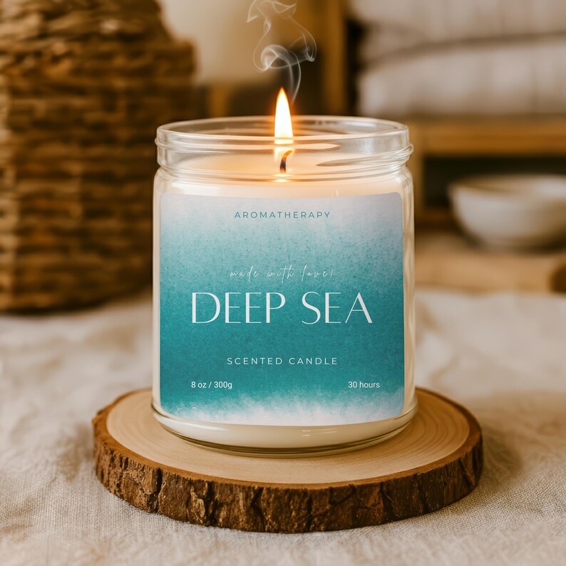 Op de afbeelding: Een brandende geurkaars in een glazen pot met het opschrift "Deep Sea". Het etiket heeft een turquoise en witte gradi&euml;nt ontwerp. De kaars staat op een houten onderzetter. De kaars is gelabeld met "Aromatherapie" en "Geurkaars".