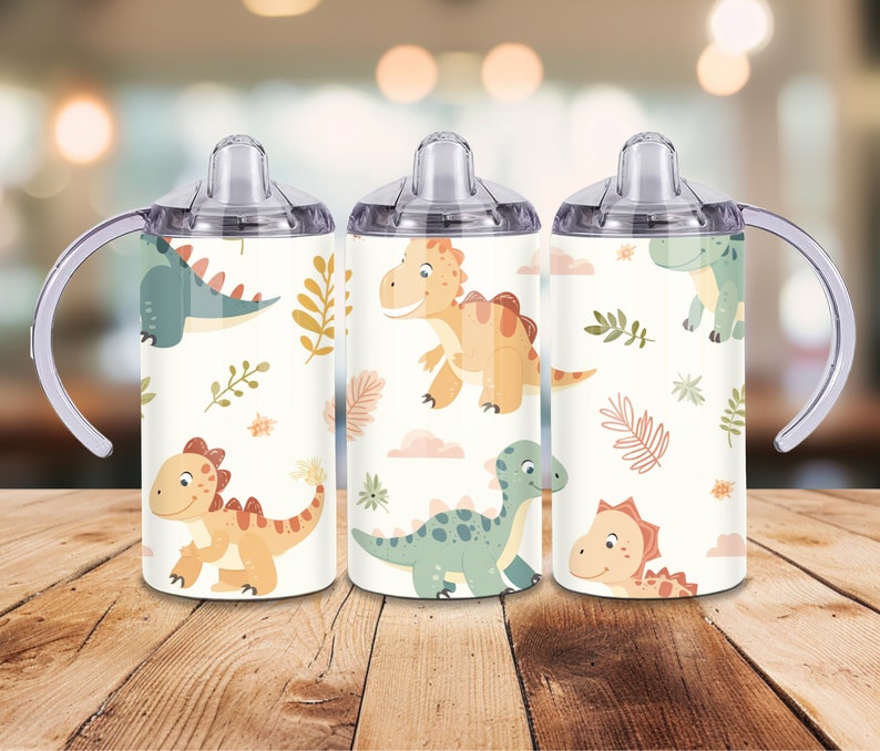Peut inclure: Trois gobelets &agrave; bec blancs avec des poign&eacute;es et des couvercles transparents. Chaque gobelet pr&eacute;sente un motif r&eacute;p&eacute;t&eacute; de dinosaures de dessins anim&eacute;s dans des tons de vert, d'orange et de jaune, ainsi que des nuages roses et des feuilles marron. Les gobelets sont con&ccedil;us pour les enfants.