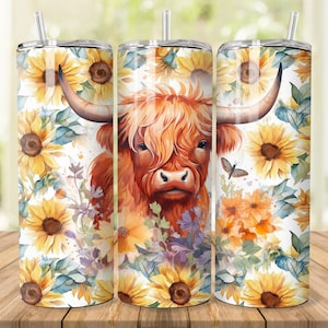 Puede incluir: Tres vasos de acero inoxidable con un dise&ntilde;o de una vaca Highland de pelaje marr&oacute;n y cara blanca, rodeados de girasoles y otras flores. Los vasos est&aacute;n sobre una superficie de madera.