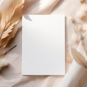 Pode incluir: Um cart&atilde;o branco em branco sobre um fundo de tecido bege com flores e folhas secas.