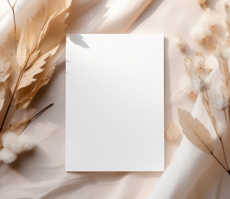 Pode incluir: Um cart&atilde;o branco em branco sobre um fundo de tecido bege com flores e folhas secas.