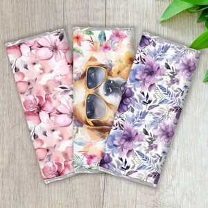 Pu&ograve; includere: Tre involucri di barrette di cioccolato con diversi disegni floreali. L'involucro centrale presenta un cane con occhiali da sole. Gli involucri sono bianchi con fiori rosa, viola e blu.