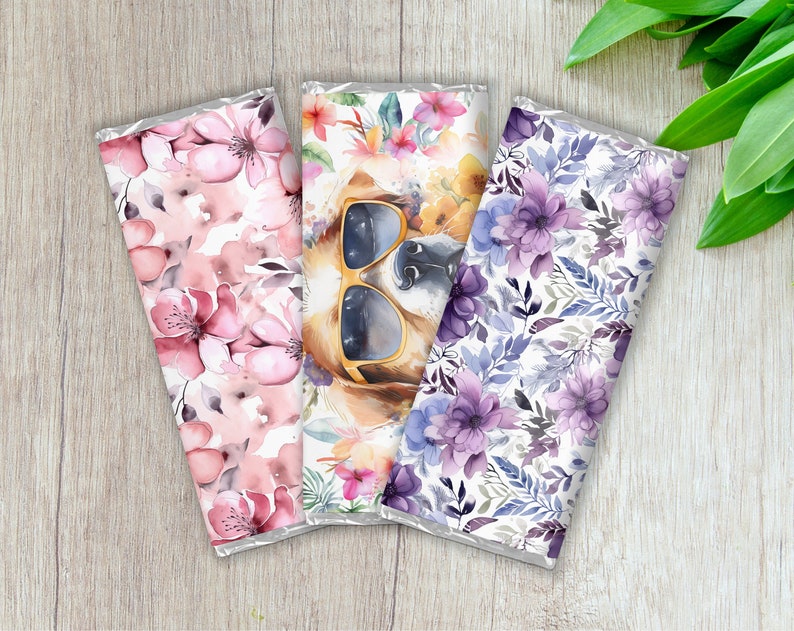 Pu&ograve; includere: Tre involucri di barrette di cioccolato con diversi disegni floreali. L'involucro centrale presenta un cane con occhiali da sole. Gli involucri sono bianchi con fiori rosa, viola e blu.