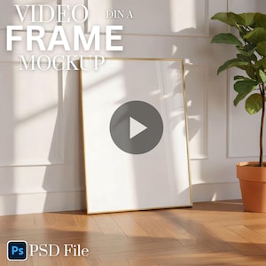 May include: A gold-framed video frame mockup leaning against a white wall. The frame has a white interior with a play button graphic. The text "VIDEO FRAME MOCKUP" is at the top. A potted plant is to the right. The bottom left corner has the text "PSD File".