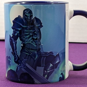 May include: A white ceramic mug with a blue handle and a blue and white image of a knight in armor holding a sword. The knight is standing in front of a blue and white background.