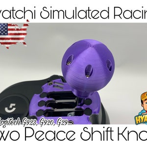 May include: Purple two-piece shift knob for Logitech G923, G920, G29 racing wheels. The knob has a textured surface and a small, round top. The knob is attached to a black shifter base.