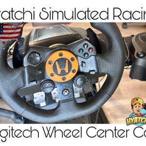 May include: Black Logitech racing wheel with an orange center cap featuring a logo. The wheel has various buttons and controls. The image includes the text "Hyatchi Simulated Racing" and "Logitech Wheel Center Cap".