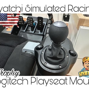 Puede incluir: Una palanca de cambios negra con una perilla texturizada montada en un Playseat Logitech. La palanca de cambios está etiquetada como "Trophy" y forma parte de una configuración de carreras simuladas. La imagen también incluye una pequeña bandera estadounidense y el texto "Hyatchi Simulated Racing".