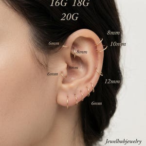 May include: A collection of thin gold hoop earrings worn in multiple ear piercings. The image includes text labels for gauges 16G, 18G, 20G and diameters 6mm, 8mm, 10mm, and 12mm. The text Jewelhubjewelry is visible in the bottom right corner.