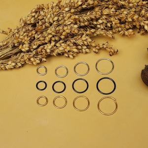 May include: A set of 10 hoop earrings in three different sizes and colors: gold, silver, and black. The hoops are arranged in three rows on a light brown surface.