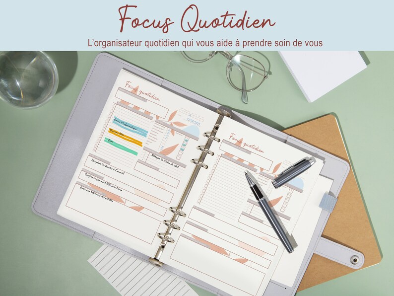 May include: A gray and white daily planner with a ring binder. The planner has the words "Focus Quotidien" and "L'organisateur quotidien qui vous aide &agrave; prendre soin de vous" printed on the cover. The planner is open to a page with the words "Face quotidien" printed at the top.