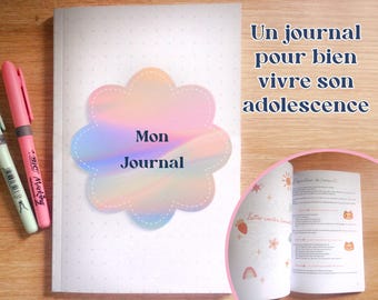 May include: A journal with the text "Mon Journal" on the cover, featuring a pastel rainbow design. The journal is open to reveal interior pages. Two pens, one pink and one light green, are placed on the left side of the journal.