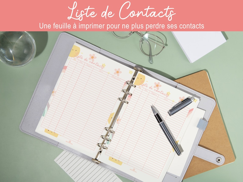 Peut inclure: Un classeur gris avec deux pages ouvertes, chaque page a une grille rose et blanche avec le texte "Liste de contacts" en haut. Les pages sont d&eacute;cor&eacute;es d'un soleil jaune et de fleurs roses. Un stylo argent&eacute; est pos&eacute; sur la page de droite.