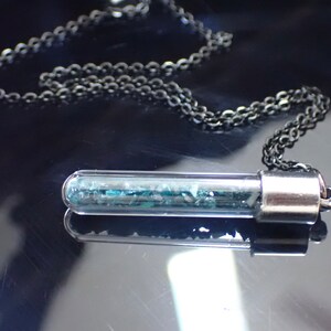 May include: A silver necklace with a clear glass tube pendant filled with teal glitter. The tube has a silver cap on one end.