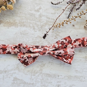 May include: A red and white bow tie with a floral pattern. The bow tie is made of fabric and has a classic shape.