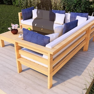 May include: Outdoor sectional sofa with a light wood frame and white cushions. The sofa has blue throw pillows and a matching coffee table. A small vase of flowers and a cup of coffee are on the table.