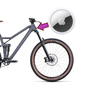 以下が含まれることがあります： 黒とオレンジのフォークが付いたグレーのマウンテンバイク。自転車は、前面に白い「140R」ロゴが付いた黒いフレーム。自転車は、側面に白い「SCHWALBE」ロゴが付いた茶色のタイヤ。自転車には、ハンドルバーに黒と白のApple AirTagが取り付けられています。