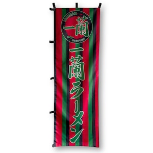 May include: A red and green striped banner with Japanese text that reads "Ichiran Ramen" and a circle with the text "Ichiran" in Japanese. The banner is hanging from black straps.