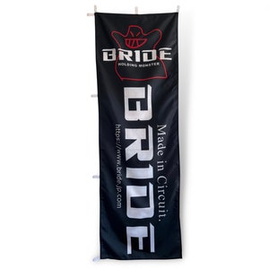 Puede incluir: Pancarta negra con texto blanco que dice "BRIDE" y "Made in Circuit." El texto está en una fuente grande y en negrita. Debajo del texto hay una fuente blanca más pequeña que dice "https://www.bride.jp.com". La parte superior de la pancarta presenta un fantasma de dibujos animados rojo con el texto "HOLDING MONSTER" en rojo.