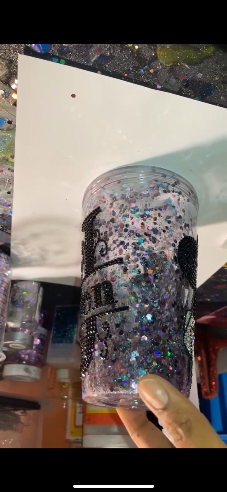 May include: A clear plastic tumbler with a black glitter design and the words "Bad to the Bone" written in black. The tumbler is filled with iridescent glitter.