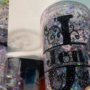 May include: A clear plastic tumbler with a black glitter design and the word "Jen" in black lettering.