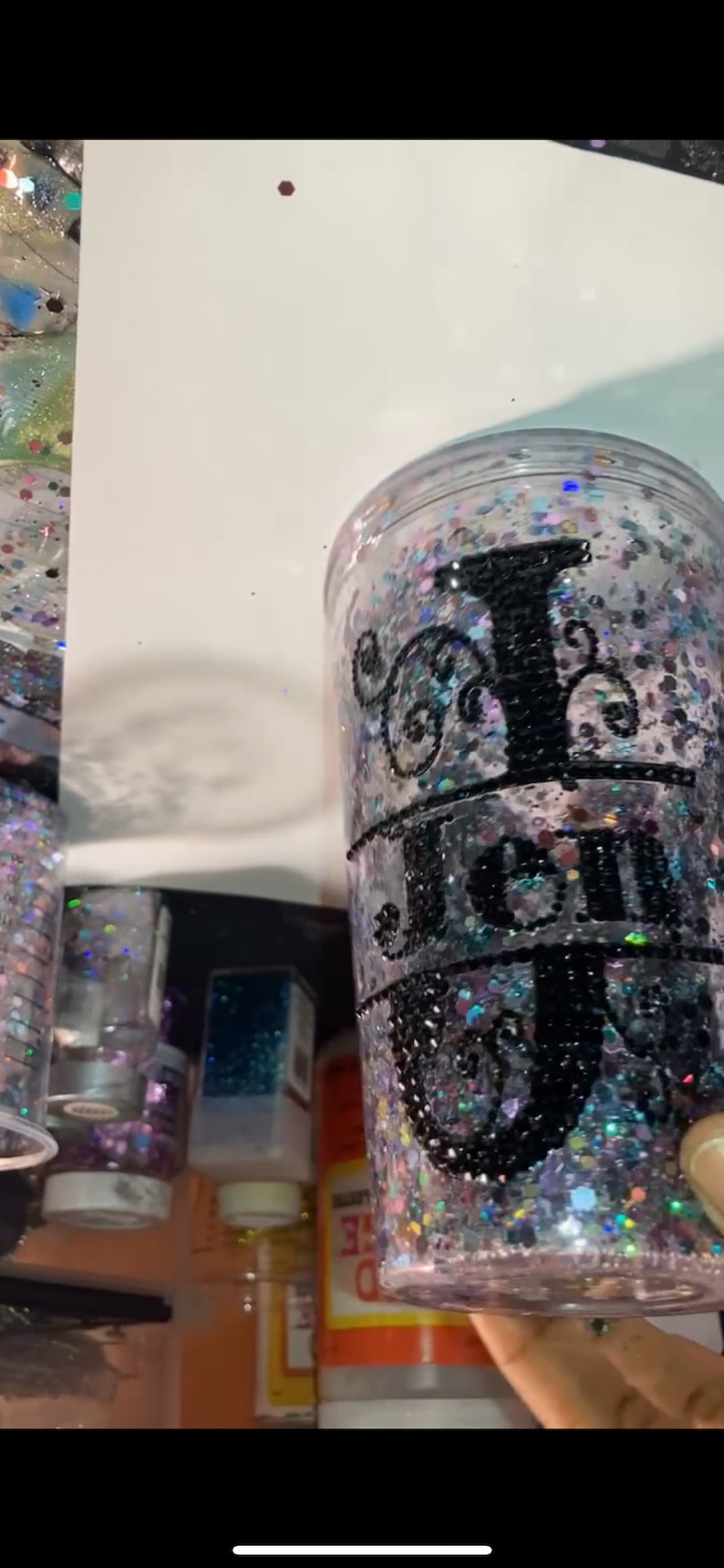 May include: A clear plastic tumbler with a black glitter design and the word "Jen" in black lettering.