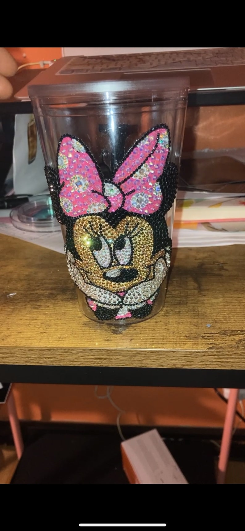 May include: A clear plastic tumbler with a rhinestone design of Minnie Mouse. The design features a pink bow with white polka dots and black ears.