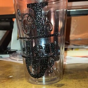 May include: A clear plastic tumbler with a black rhinestone design that says "I Just Got Real".