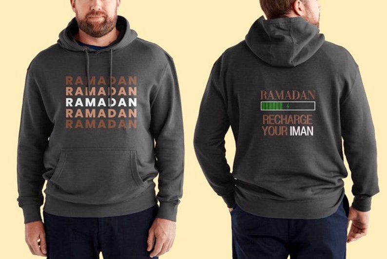 Puede incluir: Una sudadera con capucha gris oscuro con un bolsillo en la parte delantera. La parte delantera de la sudadera tiene la palabra "RAMADAN" repetida cinco veces en un patr&oacute;n apilado. La parte posterior de la sudadera tiene las palabras "RAMADAN RECHARGE YOUR IMAN" con una barra de progreso verde debajo de la palabra "RAMADAN".