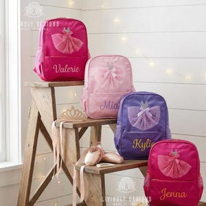 May include: Four backpacks in pink, light pink, and purple, each with a tutu design and a name embroidered on the front. A wooden step stool holds the backpacks, a tiara, and ballet shoes. The backpacks have side pockets.