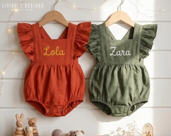 May include: Two sleeveless rompers with ruffled shoulders, one in rust orange with the embroidered name Lola and one in olive green with the embroidered name Zara. Both garments feature a square neckline and a gathered bottom with snap closures.