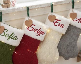 May include: Four knit Christmas stockings with white faux fur cuffs, each personalized with embroidered names Sofia, Evelyn, Eva, and a partial name. Each stocking features a hanging heart-shaped brown paper tag and a green fabric loop.