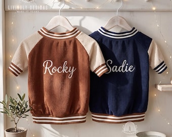 May include: Two short-sleeved ribbed shirts hanging on hangers. The left shirt is brown with cream sleeves and the name Rocky in white script. The right shirt is navy blue with cream sleeves and the name Sadie in white script. Both have striped trim.