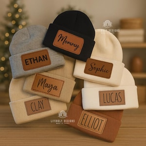 May include: A selection of beanies in shades of grey, black, beige, and brown. Each beanie has a rectangular leather patch with names like "Ethan" and "Lucas". The word "Mommy" is also displayed on a black beanie.