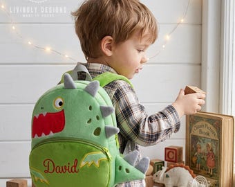 May include: A light green plush dinosaur backpack featuring a red mouth, grey spikes, and the name David embroidered in red on the front pocket. The backpack has a zipper closure and adjustable straps, designed with a soft, textured fabric.