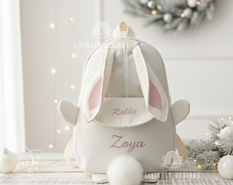 May include: A white rabbit-shaped backpack with pink inner ears and a fluffy tail. The backpack has the name "Zoya" embroidered in pink script below the word "Rabbit". The bag has a top handle and adjustable straps.