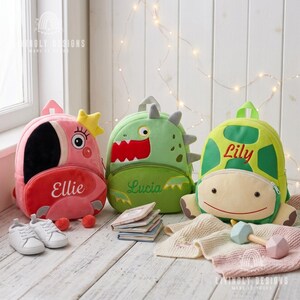 May include: Three plush backpacks featuring animal designs: a pink flamingo with the name Ellie, a green dinosaur with the name Lucia, and a green turtle with the name Lily. Each bag has a front zippered pocket and embroidered personalisation.