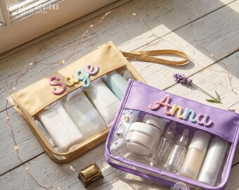 May include: Two rectangular zippered pouches with clear front panels and wrist straps. One pouch is beige with the name Sage in pastel crocheted letters, the other is lavender with the name Anna in pastel crocheted letters, both containing bottles.
