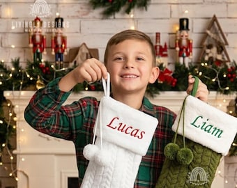 May include: Two personalized Christmas stockings with white faux fur cuffs. One stocking is white with red embroidery reading Lucas, and the other is olive green with green embroidery reading Liam. Both feature cable knit textures and pom-poms.