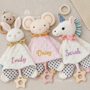 May include: A collection of plush baby comfort toys, including a bunny, mouse, and unicorn, each with a personalized name embroidered on the blanket. The toys feature floral accents, polka dot patterns, and star-shaped teethers.