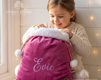 May include: A deep magenta velvet Christmas gift sack featuring a white faux fur trim at the top, red and white twisted rope drawstrings with white pom-poms, and the name Evie embroidered in white script on the front of the fabric.
