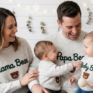 Może przedstawiać: Rodzina czteroosobowa w pasujących swetrach w kropki. Swetry mają zielone napisy "Mama Bear", "Papa Bear" i "Baby Bear" z brązową twarzą misia. Tło to biała ściana z łańcuchem świetlnym.