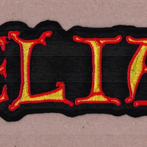 May include: A rectangular embroidered patch featuring the word BELIAL in a stylized font. The letters are filled with a gradient of yellow and orange, outlined in a bold red thread, all set against a solid black background with a black border.