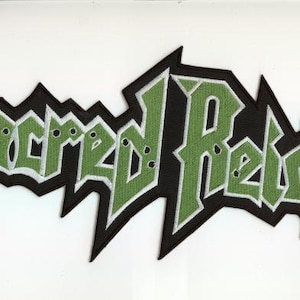 May include: Embroidered patch featuring the band name "Sacred Reich" in green letters with white outlines, set against a black jagged border. The patch is likely for a jacket or bag.