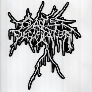 May include: An embroidered patch featuring the text Cattle Decapitation in a stylized, jagged, white font with a black border. The lettering is intricate and sharp, resembling branches or roots, creating a dense, organic, and chaotic visual design.