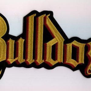 Pode incluir: Patch bordado com a palavra "Bulldozer" em fonte gótica. O texto é dourado com contorno vermelho e borda preta. Adequado para roupas ou acessórios.