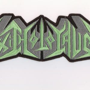 Puede incluir: Parche bordado con la palabra "ASPHYXIOUS" en una fuente estilizada y angular. El texto es verde claro, delineado en gris y sobre un borde negro. El parche tiene una forma única y dentada.
