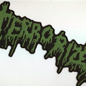 May include: A black patch with the word "TERRORIZER" in dripping green letters. The patch has a jagged, irregular shape and is likely designed to be sewn or ironed onto clothing or accessories.