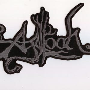 May include: A black patch with the word "Afrood" in a stylized, gray font. The patch has a unique, organic shape with a gray border, set against a white background. The design is likely for clothing or accessories.